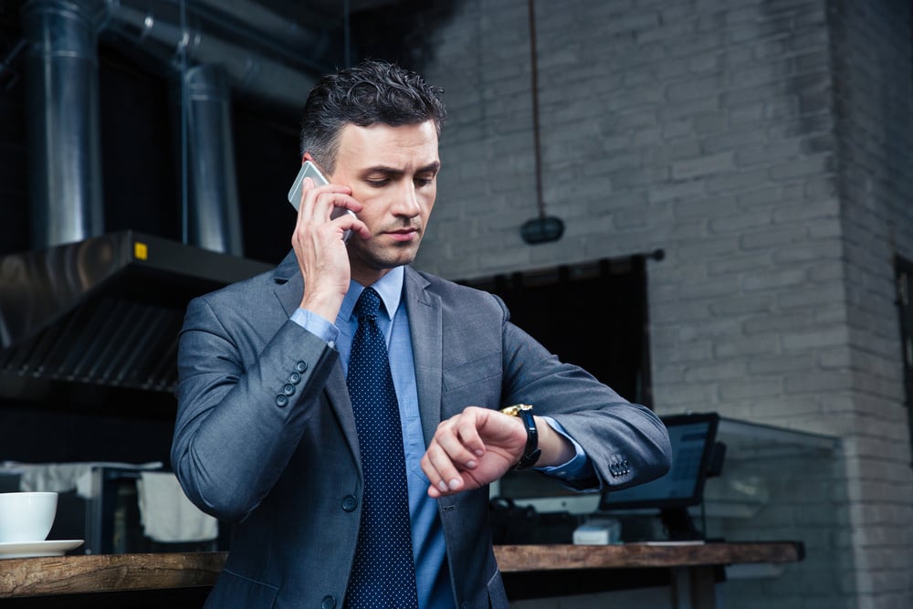 Confident businessman speaking on the phone and looking on the wristwatch in cafe