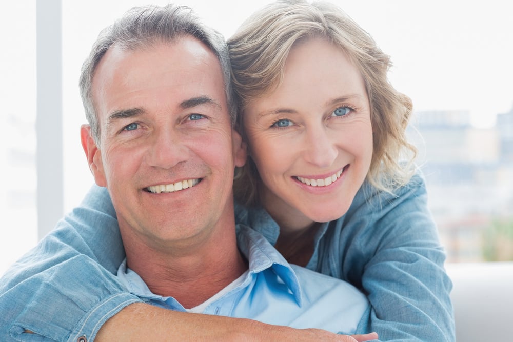 Smiling woman hugging her husband on the couch from behind at home in the living room